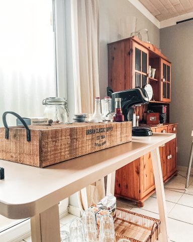 Holztisch mit Glasbehältern und Küchenutensilien vor einem Fenster und einem Schrank.