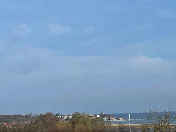 Heller Himmel über einer Küstenlandschaft mit Häusern und Wasser im Hintergrund.